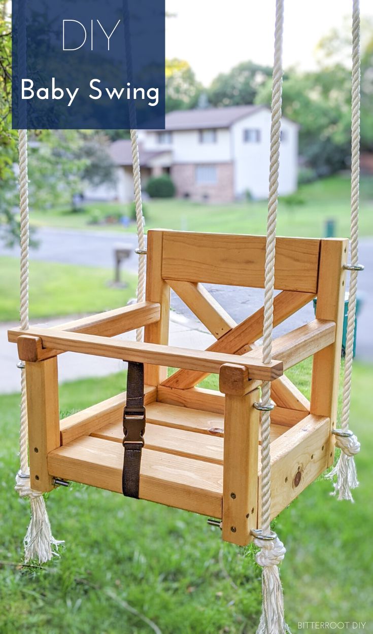 a wooden swing hanging from a tree in the grass