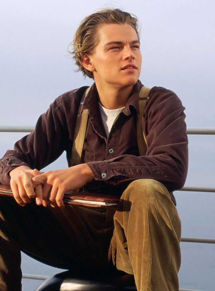 a young man sitting on top of a wooden bench next to the ocean with his arms crossed