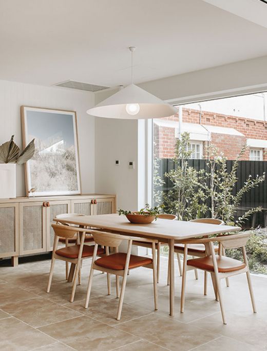 a dining room table with four chairs and a potted plant in the center, next to an open window