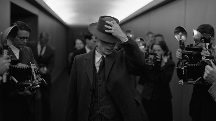 a man in a suit and hat walking down a hallway with cameras around him,