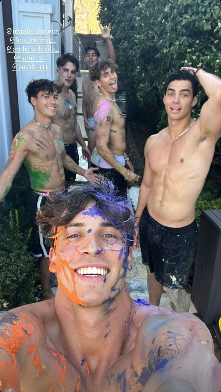 a group of young men standing next to each other in front of a house covered in paint