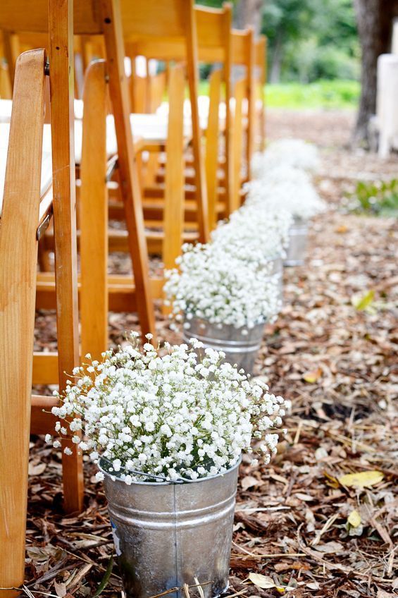 three buckets filled with white flowers sitting on the side of a wooden chair line