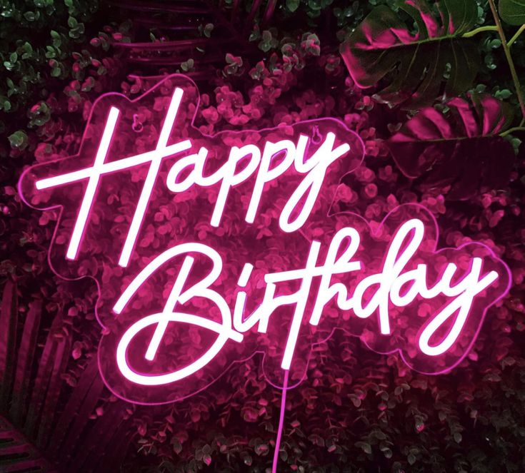 a neon sign that says happy birthday in front of some plants and flowers on the wall