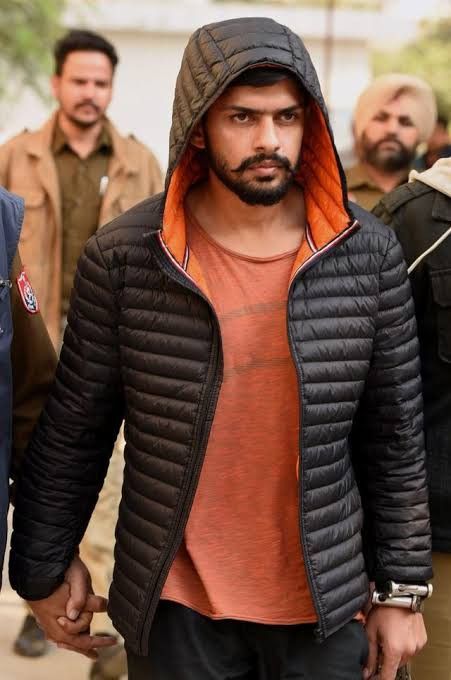 a man in a black jacket and orange shirt is walking with other men behind him