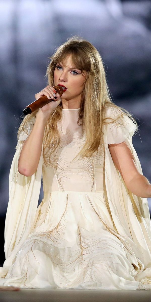 a woman in white dress holding a microphone to her mouth while sitting on a stage