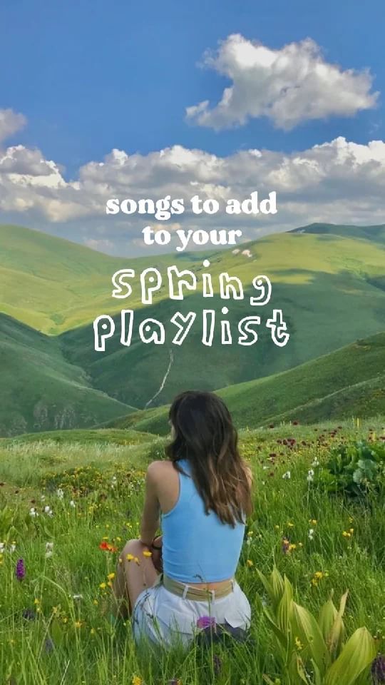 a woman sitting on top of a lush green field next to a mountain covered in flowers