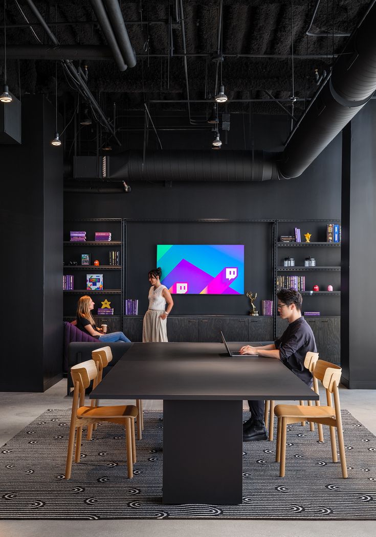 two people are sitting at a table in an office with black walls and flooring