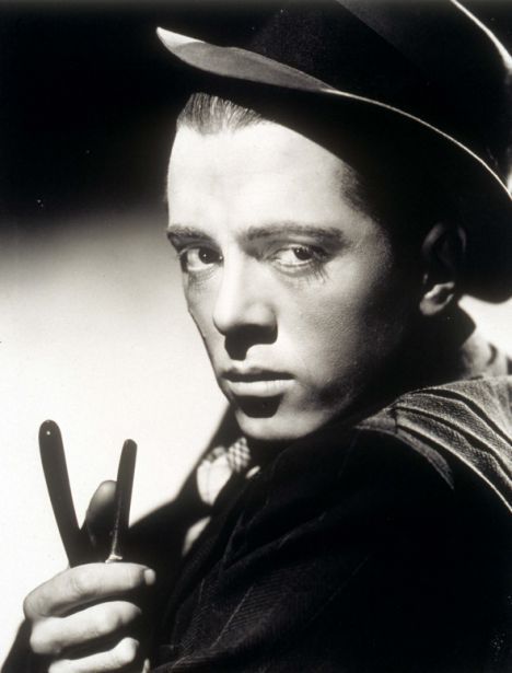 black and white photograph of a man wearing a fedora holding a pair of scissors