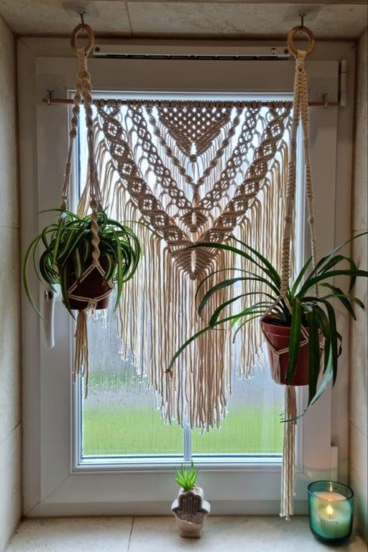 two potted plants in front of a window with macrame hanging from it