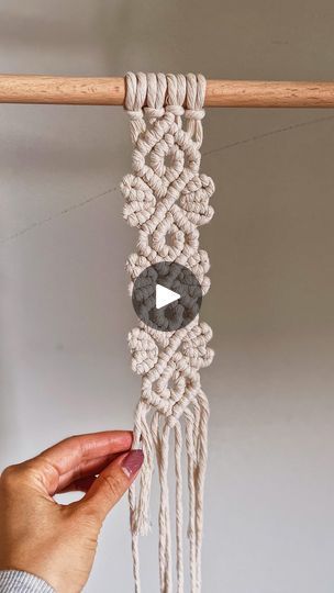 a person is holding up a macrame with an arrow in the middle and two beads on each end