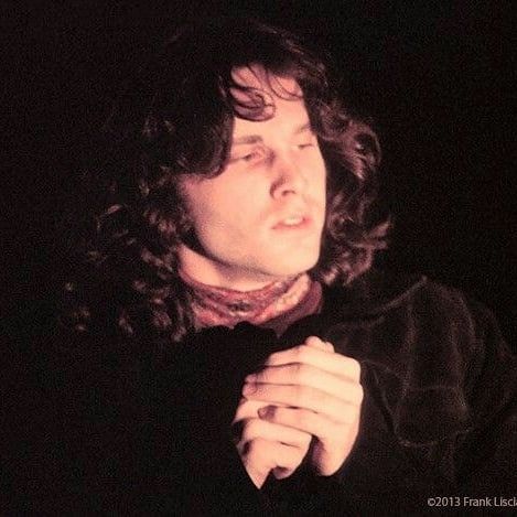 a man with long curly hair wearing a black jacket and bow tie in the dark