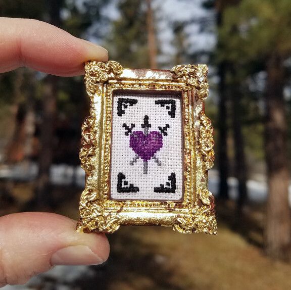 someone is holding up a cross - stitch picture frame with a heart in the middle