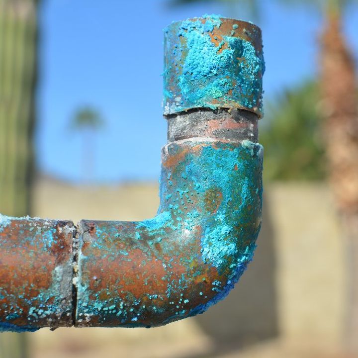 an old rusty pipe sticking out of the ground next to a cactus in front of a blue sky