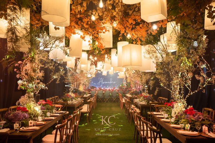 a long table with lots of flowers and paper lanterns hanging from it's ceiling