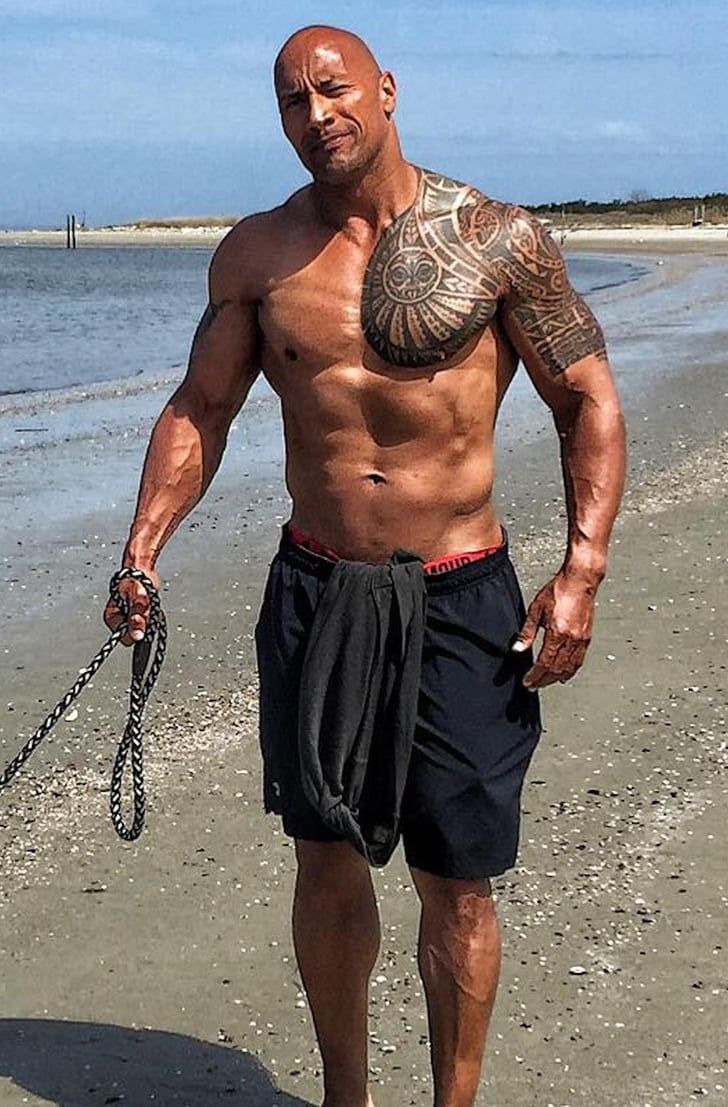 a man walking on the beach with a chain attached to his chest and wearing no shirt