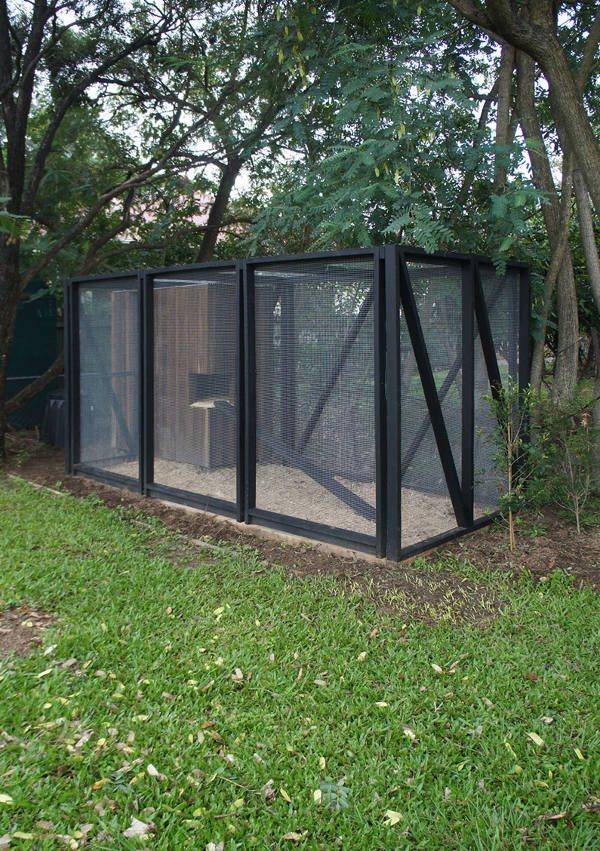 a small cage in the middle of a grassy area with trees and bushes behind it