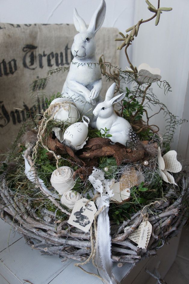 two white rabbits sitting on top of a nest filled with moss and shells in front of a pillow