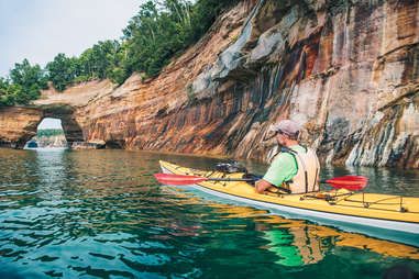 a man is paddling his kayak in the water near a cliff and waterfall