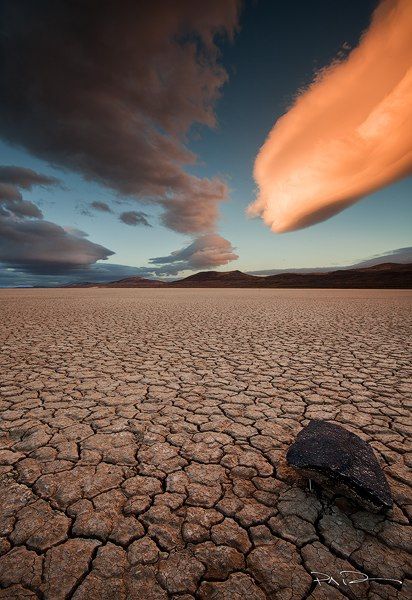 a rock sitting on top of a dry grass covered desert field under a cloudy sky