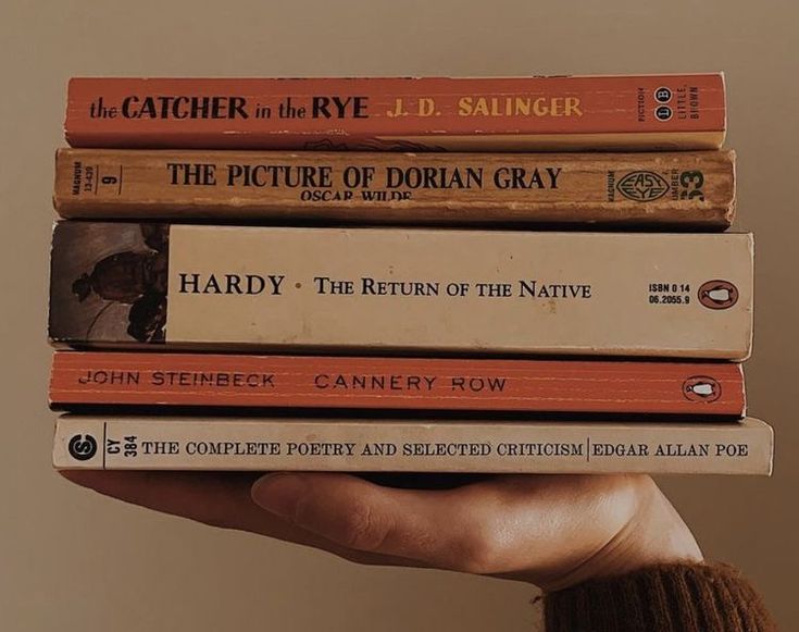 a person holding a stack of books on top of each other in front of a wall