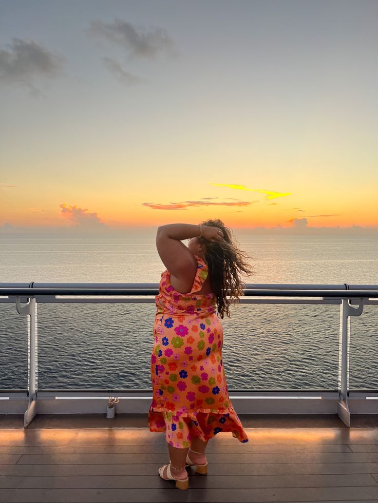a woman standing on the deck of a cruise ship looking out at the ocean as the sun sets