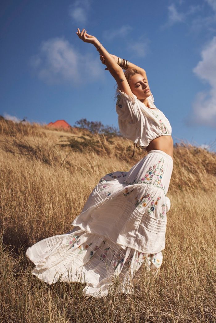 a woman in a white dress is standing in the grass and stretching her arms up