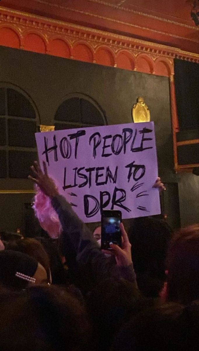 a person holding up a sign in front of a crowd with cell phones and other people