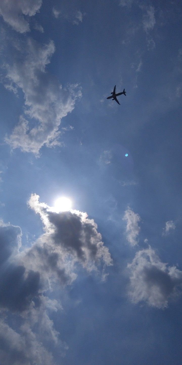 an airplane is flying through the blue sky with white clouds and sun in the background