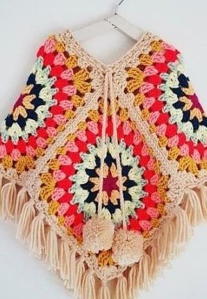 a colorful crocheted shawl hanging on a white wall with tassels