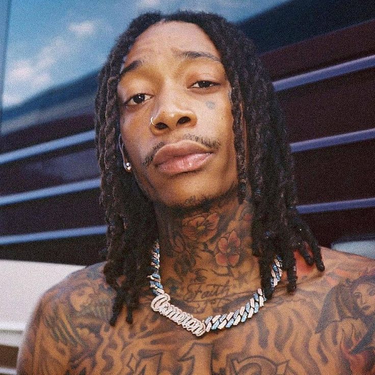 a man with tattoos on his chest wearing a chain around his neck and holding a cell phone to his ear