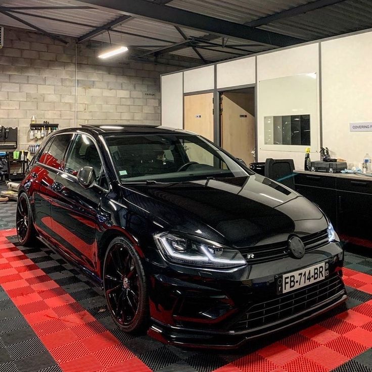 a black car parked in a garage with red and white checkered flooring on the ground