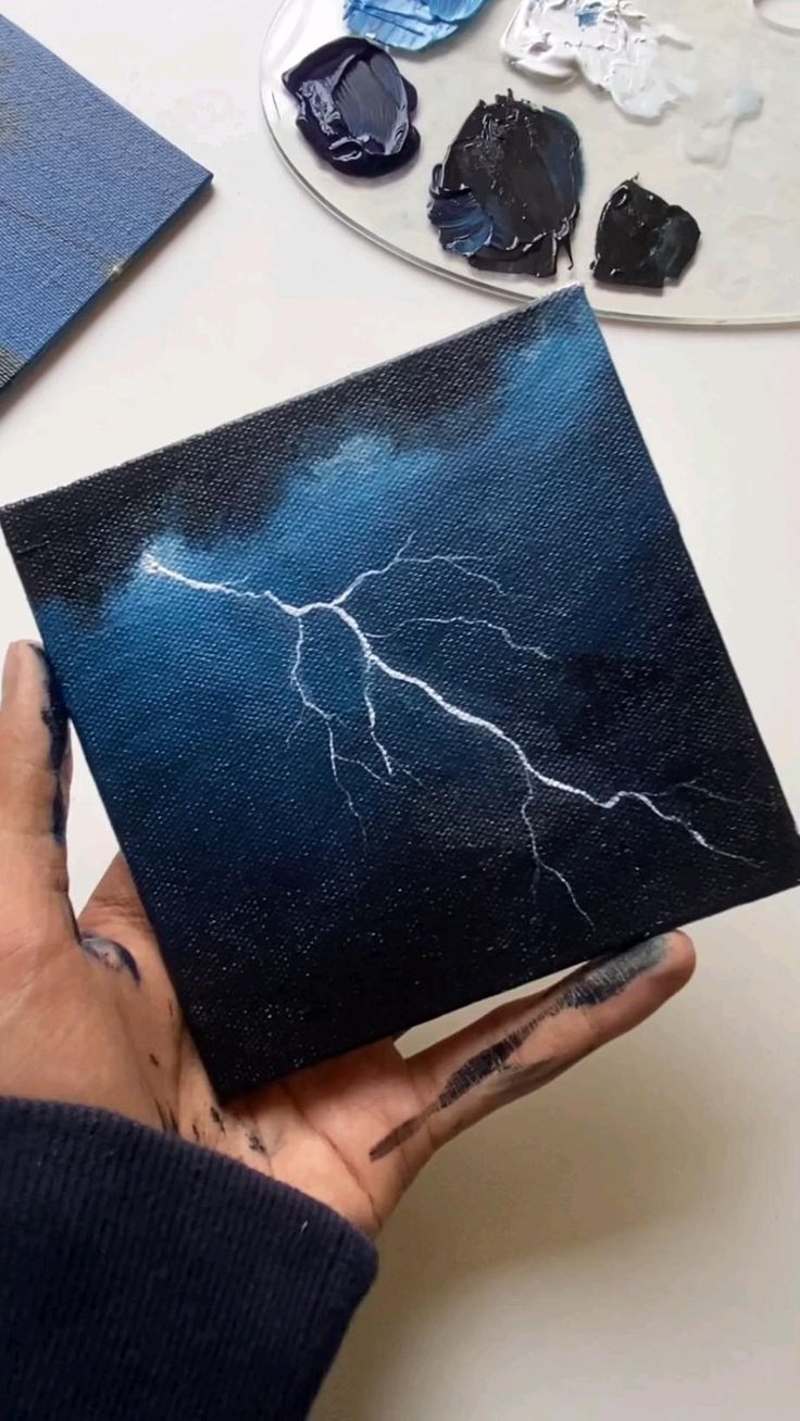 a person holding up a piece of art that has a lightning painting on it