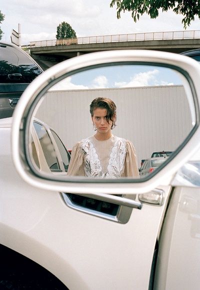 a woman is reflected in the rear view mirror of a white car while standing outside