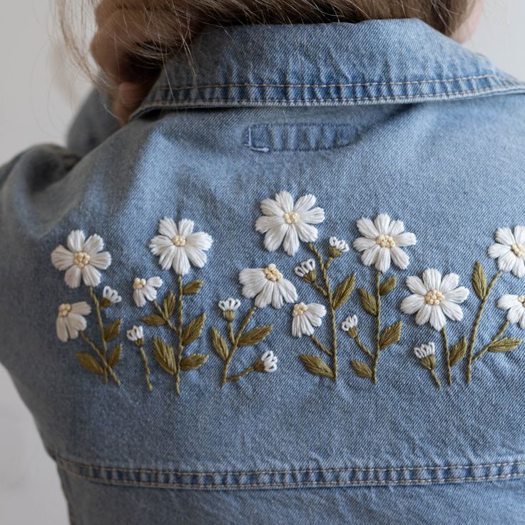 the back of a woman's jean jacket with white flowers embroidered on her chest
