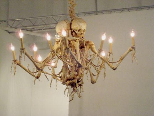 a skeleton chandelier hanging from the ceiling with lit candles in front of it