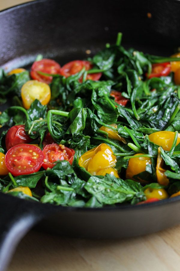 spinach and tomatoes are cooking in a skillet