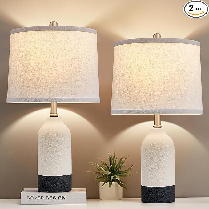 two white and black ceramic lamps on top of a table next to a potted plant