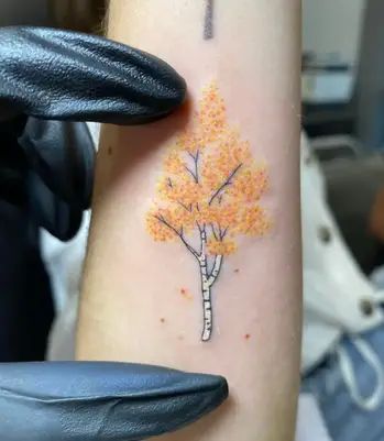 a person with a tattoo on their arm holding up a cross and an orange tree