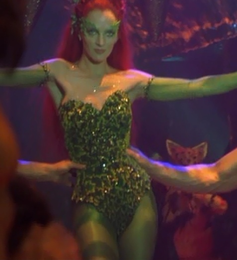 a woman in a green bodysuit with her arms spread out and two hands behind her back