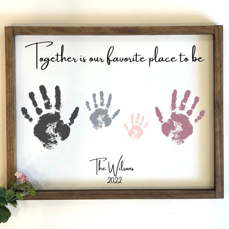 two handprints are displayed in a frame on the wall next to a plant