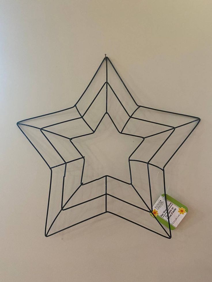 a wire star hanging on the wall with a tag attached to it's side