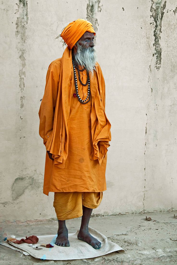 an old man standing in front of a white wall wearing a yellow turban