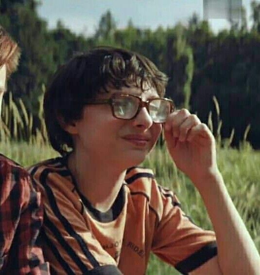 two young boys sitting next to each other in front of some tall grass and trees