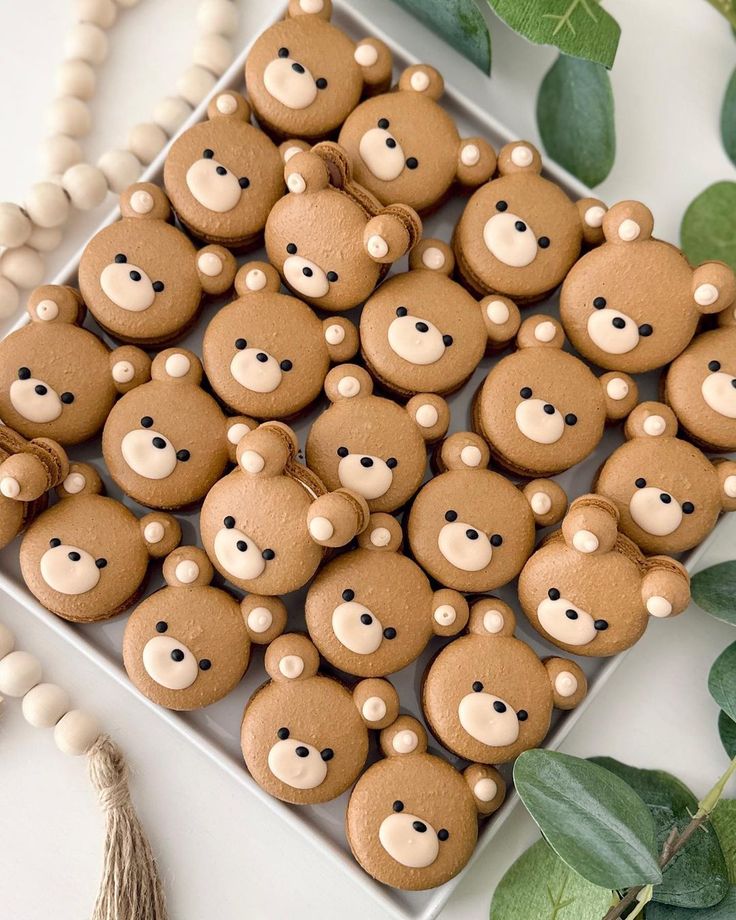 cookies decorated with teddy bears and tassels are on a plate next to green leaves