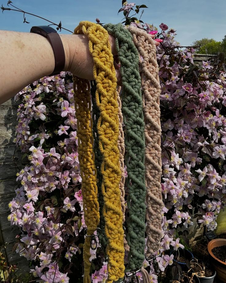 a hand is holding several crocheted bracelets in front of purple and yellow flowers