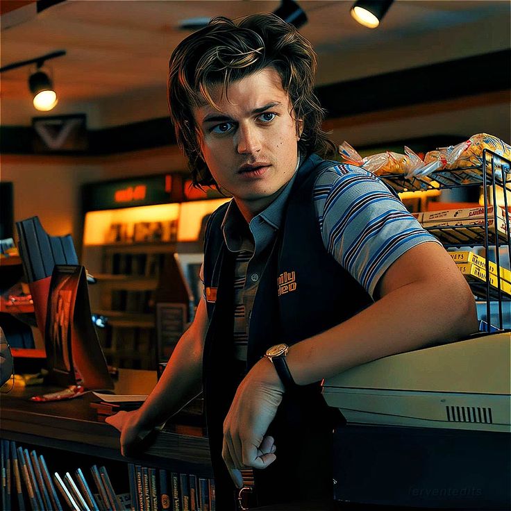 a young man standing in front of a counter with lots of items on it and looking at the camera