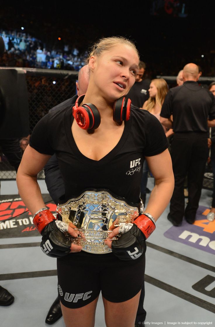 a woman standing in a boxing ring with headphones on her ears and holding a belt