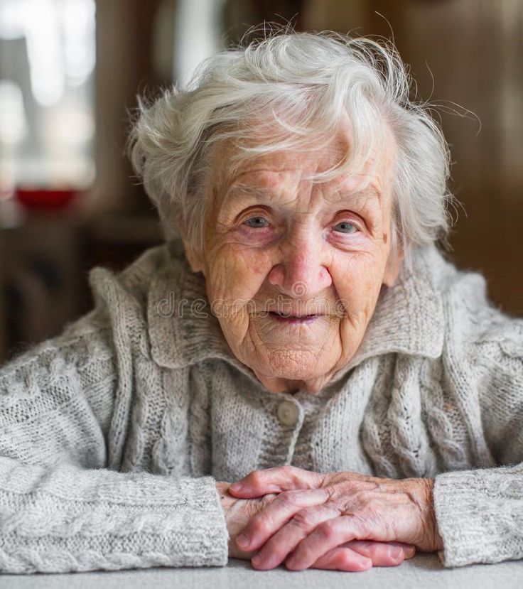 an older woman sitting at a table with her hands on her chest and looking off to the side