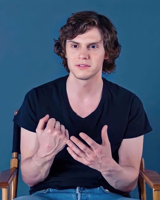 a young man sitting in a chair with his hands folded up and looking at the camera