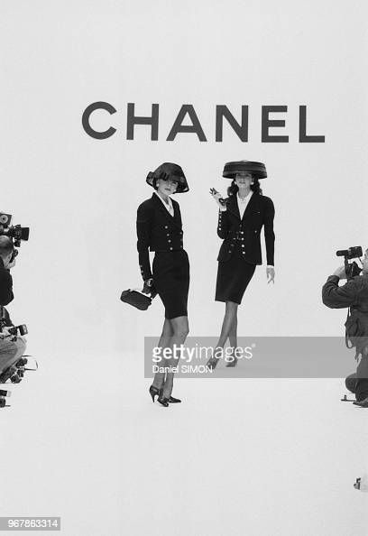 two women are standing in front of a chanel sign with cameras around them and taking pictures